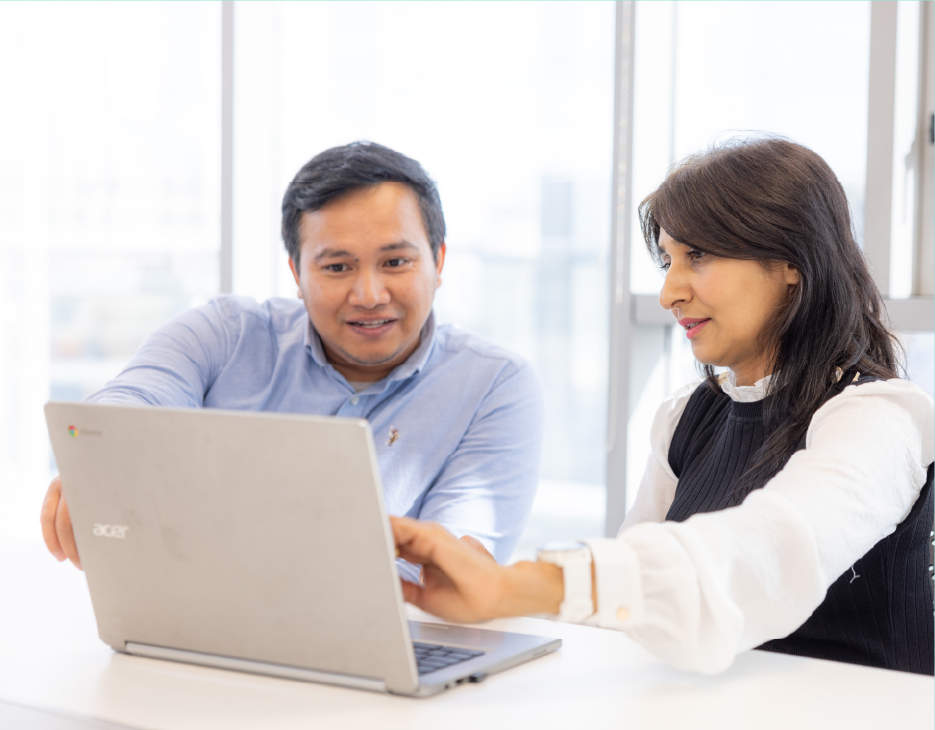 Male and female in an office environment reviewingcontent on a laptop. Content is not visible.