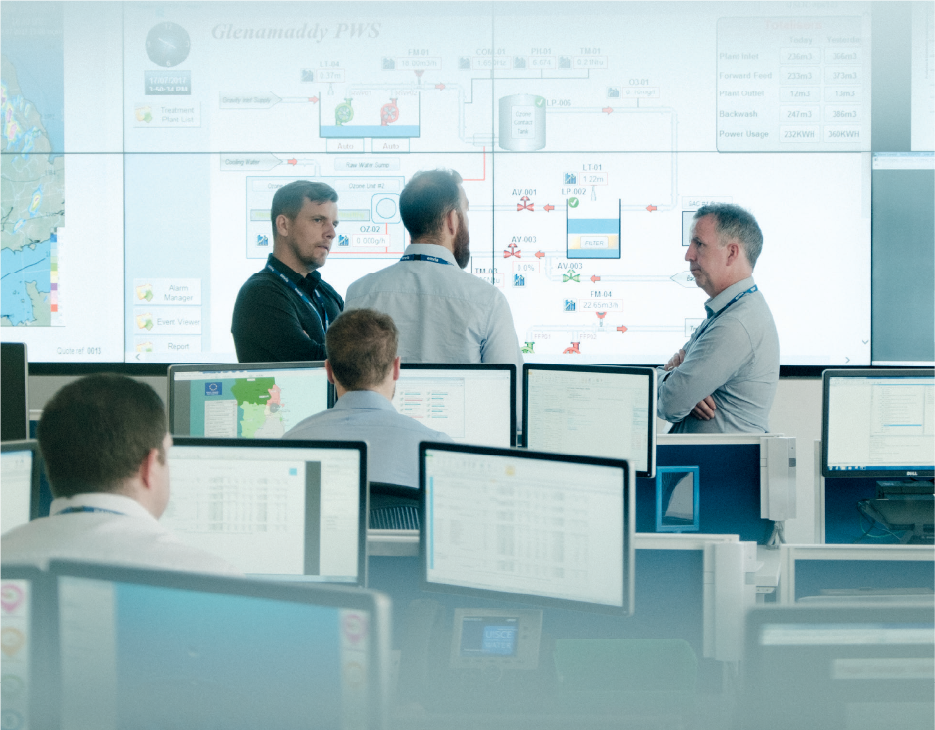 3 males standing in front of multiple large screens depicting a waterworks schematic.