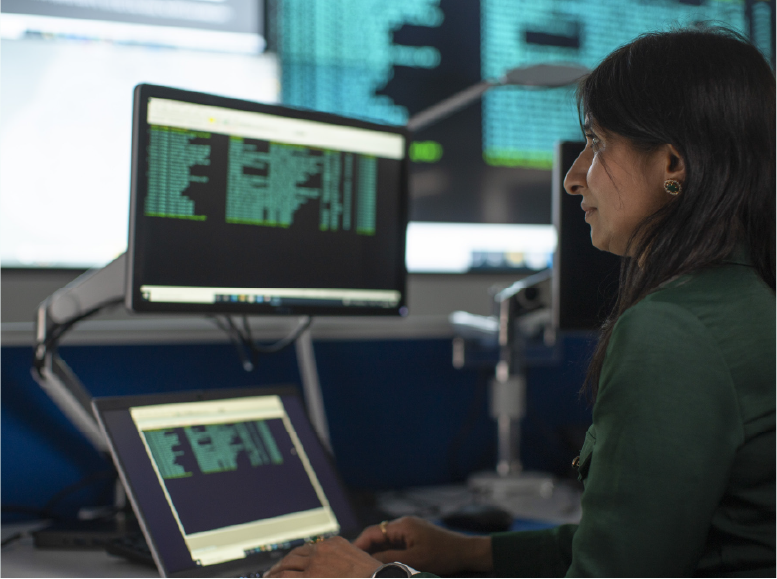 Woman with laptop and connected additional screen at eye level in an offie environment.