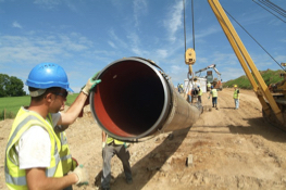 An Uisce Éireann worker with his hand on a large pipe on a construction site