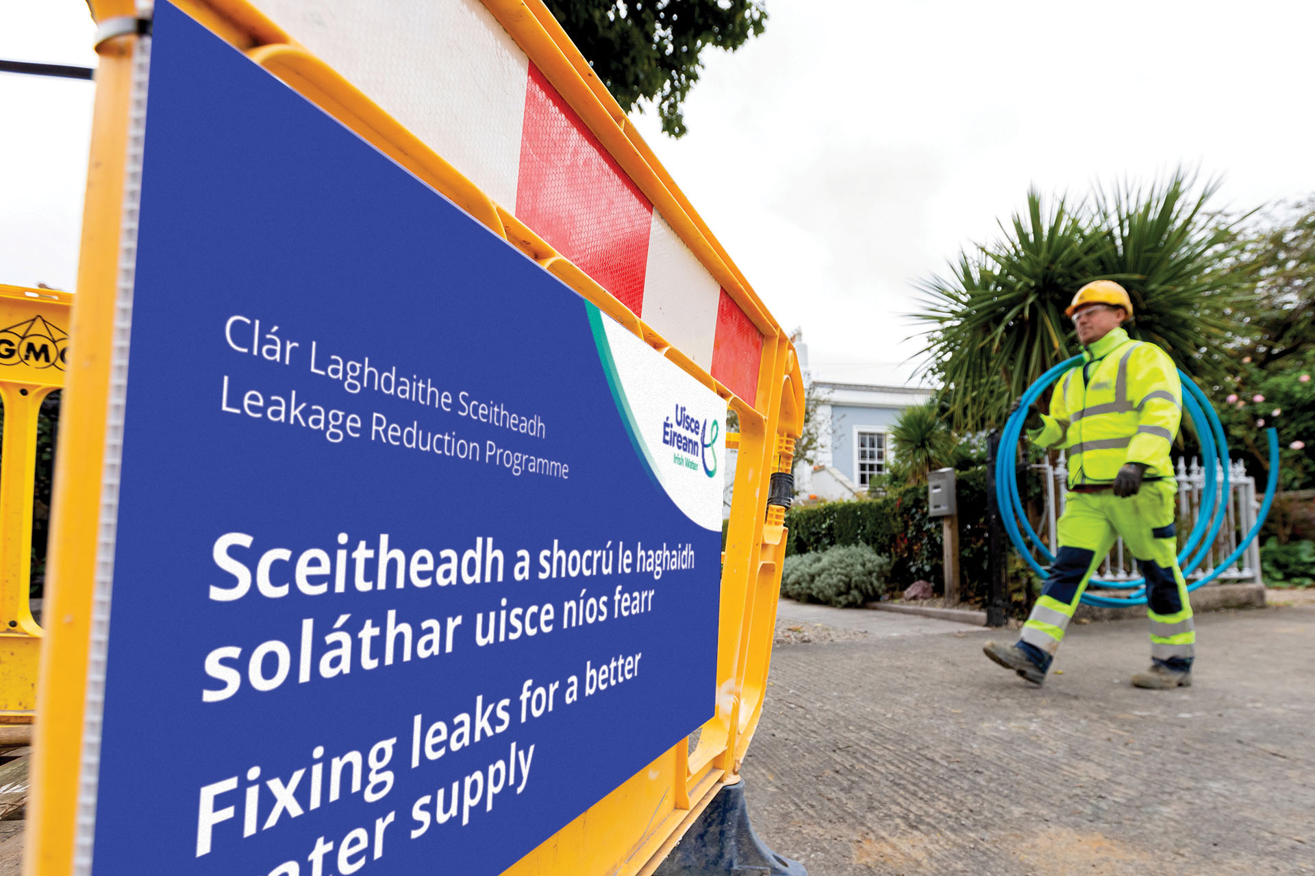 Uisce Éireann carrying a rolled up plastic blue pipe walking across an Uisce Éireann signage about fixing leaks