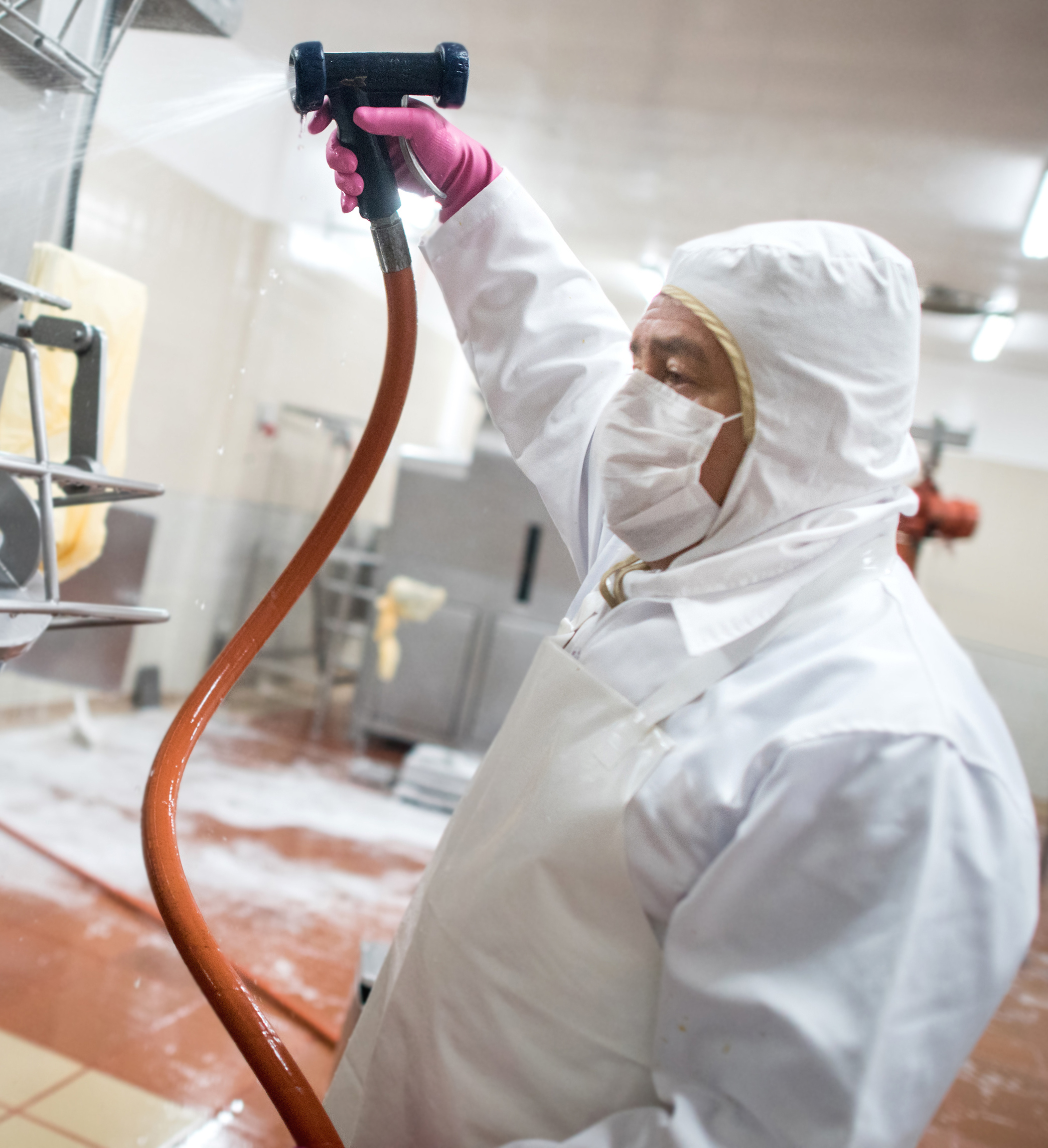 A man washing machines with a hose in a factory