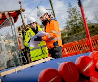 Two Uisce Éireann engineers doing road works with pipes looking at plans