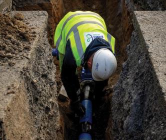 An Uisce Éireann worker fixing a blue pipe in the ground